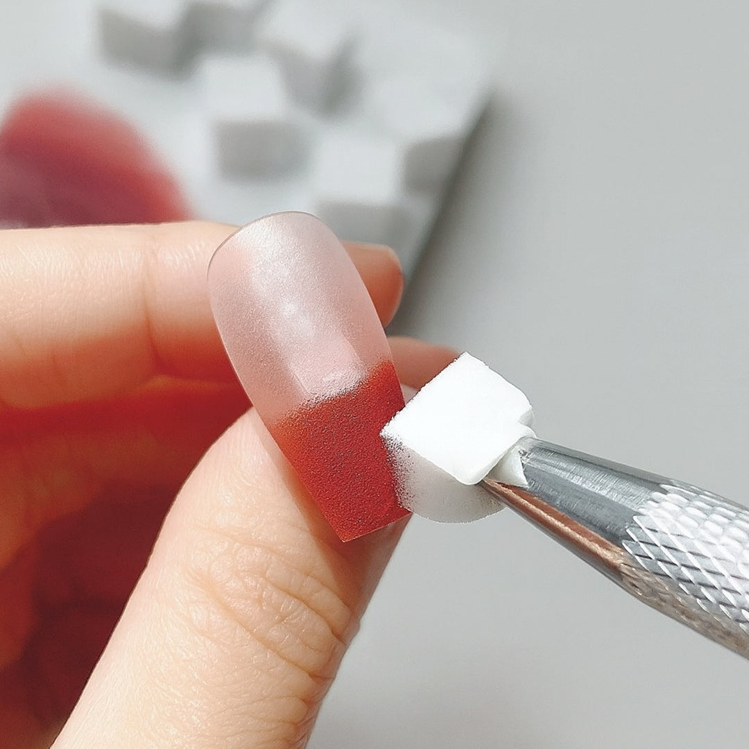 Sponge tool applying ombre design to a nail with red polish.