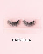 Pair of false eyelashes in a clear packaging with 'GABRIELLA' branding on a pink background.