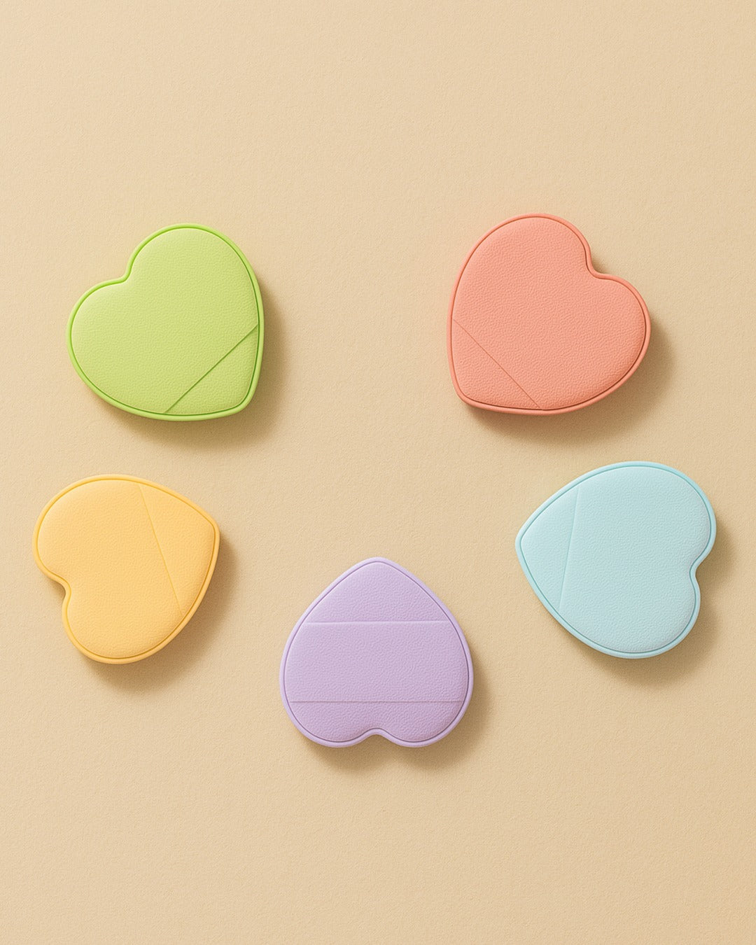Ruby Beauty heart-shaped powder puffs in pastel colors — green, orange, pink, lavender, and blue — arranged on a beige background.