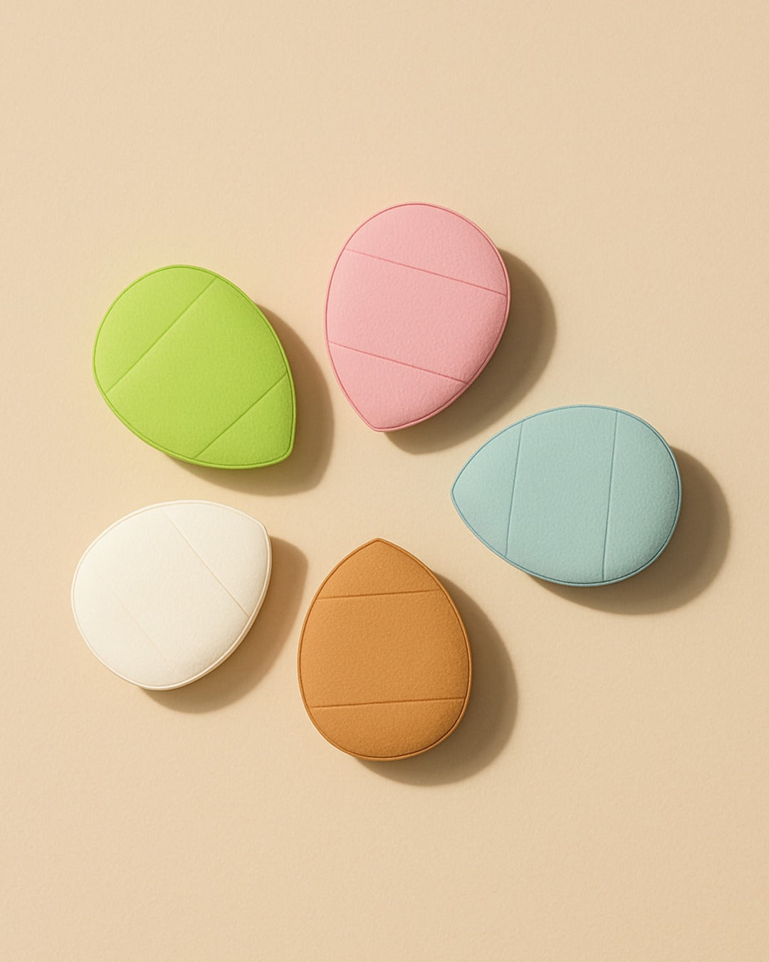 ruby Beauty teardrop-shaped powder puffs in assorted pastel colors — green, pink, white, tan, and blue — displayed on a beige background.
